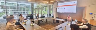 Cluster participants are sitting at a round table in the light-filled Place of Many Trees. There is screen projection with the UBC Global History of Anticolonial Thought website on it.