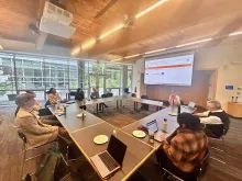 Cluster participants are sitting at a round table in the light-filled Place of Many Trees. There is screen projection with the UBC Global History of Anticolonial Thought website on it.